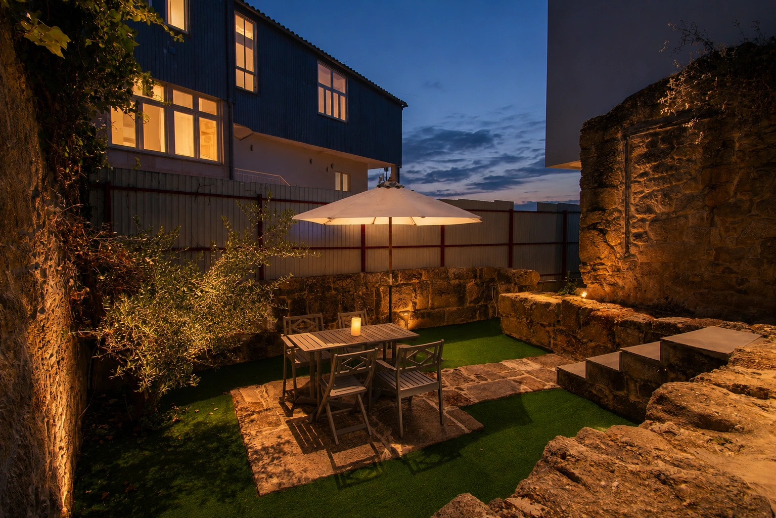 Patio exterior con mesa y sombra, zona de estar entre muros de piedra